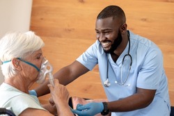 African american male health worker helping caucasian senior woman to use oxygen mask. Medical care and retirement senior lifestyle concept