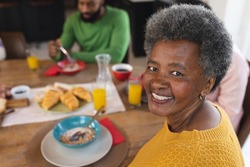 Image of happy african american senior woman eating breakfast with family. Family and spending quality time together concept.