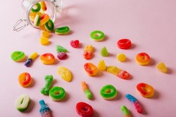 High angle view of scattered fallen colorful sugar candies with open jar on pink background. unaltered, unhealthy eating and sweet food concept.