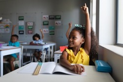 African american elementary school students with hands raised sitting at desk in classroom. unaltered, education, childhood, learning and school concept.