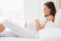 Happy pregnancy sitting on sofa at home in bedroom