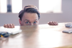 Nervous businessman peeking over desk in his office
