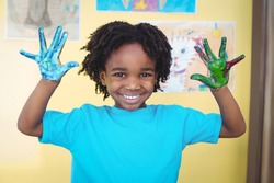 Smiling kid holding up his hands covered in paint