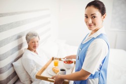 Portrait of nurse giving breakfast to senior woman in bedroom