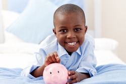Young boy smiling at the camera while putting money into his piggy bank