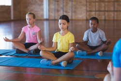 School kids meditating during yoga class in basketball court at school gym
