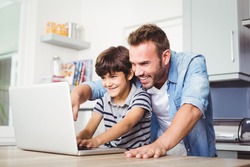Father and son using laptop on table at home