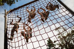 Military soldiers climbing rope during obstacle course in boot camp