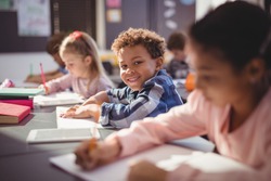 Portrait of smiling schoolboy doing his homework in classroom at school