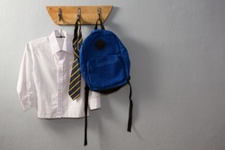 School uniform and schoolbag hanging on hook against wall