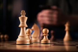 Wooden chess king on the game board. Warm atmosphere of the game. online learning. man holding phone on background