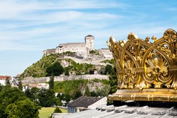 the gilded crown of the lourdes basilica and walls of the castle in the distance