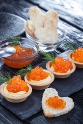 tartlets with butter and red caviar and dill on a black wooden table.