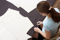 Scene in the studio for tailoring work clothes. A cutter girl works at a large table with a marker marking the fabric for further sewing of work clothes.