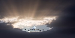 Passenger airplane flying under the storm clouds at sunset