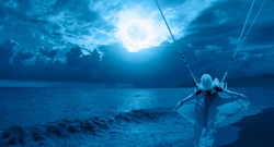 The girl riding a swing on the beach on a full moon at night 