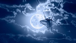 Beautiful girl riding a swing on the space on a full moon at night 