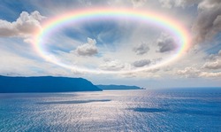Scenic sky cloudscape with big bright rainbow above sea, Blue mountains in the background