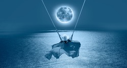 The girl riding a swing on the beach on a full moon at night 