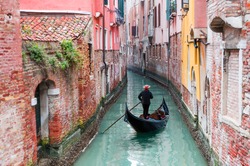 Venetian gondolier punting gondola through green canal waters of Venice, Italy