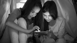 Monochrome photo of two teenage girls playing on mobile phone at night