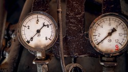 Closeup photo of two rusty manometers with analog dials connected to vintage pipes of steam engine