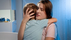 Portrait of young loving mother soothing and caressing scared little boy in children room at night. CHild being scared and crying of nightmare or bad dream.