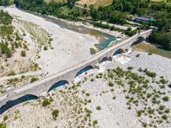 Aerial view. Drought and dry rivers. Roman bridge of Bobbio over the Trebbia river, Piacenza, Emilia-Romagna. Italy. 06-16-2022. River bed with stones and vegetation. Called hunchback bridge