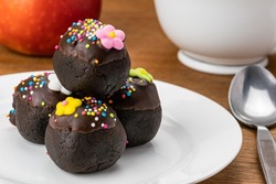 Pile of delicious homemade Choc Balls or Chocolate Balls in white ceramic dish. Delicious dessert Chocolate Balls and red ripe apple. Choc Balls topping with rainbow sprinkles and s cup of coffee.