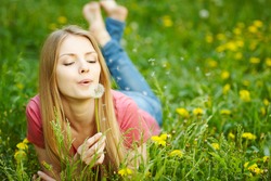 Womangirl lying on the field of dandelions blowing dandelion, wish concept