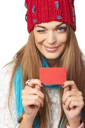 Closeup of happy smiling girl in winter hat and scarf showing blank credit card and winking you, on white background