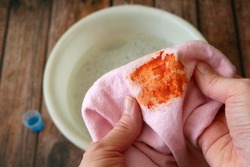 Cleaning laundry manually. Women's hands in gloves washing dirty stained on colored cloth with a stain remover and soak in soapy water, closeup