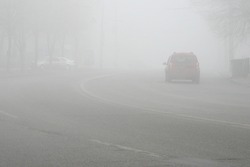 Cars in the road in city in fog. Bad winter weather and dangerous automobile traffic on the road. Light vehicles in foggy day. Outdoors