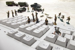 Invading force of miniature army toy soldiers in an attack on a computer keyboard as a metaphor for the risk of virus and worm infection in internet or network security