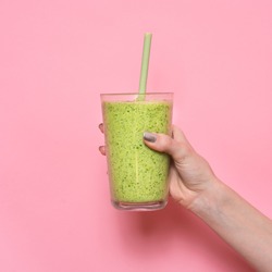 Woman hand holding smoothie shake against pink wall. Drinking green healthy smoothie concept.