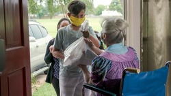 Setting a great example this mother who is part of a volunteer food delivery program takes her children along with her to deliver food to an elderly woman in a wheelchair.