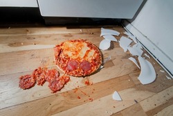 Fallen and shatter plate with food in kitchen. Dropped pizza on floor and crashed plate. Dirty environment