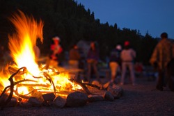 Image of a large campfire, around which people basking in the mountains at night