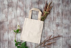 Mockup design bag concept. Top view of blank white tote bag canvas fabric with plants. White tote bag canvas fabric. Cloth shopping sack mockup with copy space. Wooden background. 