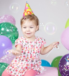Portrait of beautiful happy little girl with balloons blowing bubbles in studio