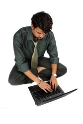 An Indian businessman sitting on a floor working on his laptop, on white studio background.