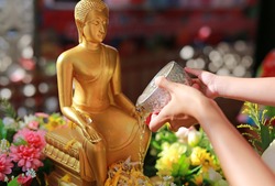 Water blessing ceremony for Songkran Festival or Thai New Year. Women and child girl paying respects to a statue of Buddha by pouring water onto it.