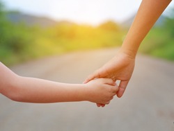 Close up of Sister hold hands with small children walking on the road with rays of sunlight.