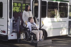 A woman in a wheelchair is helped off a van using a chair lift.