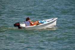 
well tanned gay man leisurely cruising in a tiny white outboard engined powered dingy.