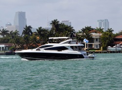 Black and white motor yacht cruising past RivaAlto Island in Miami Beach,Florida with Miami tall building skyline in the distant background.