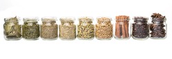 Cardamom, star anise, cinnamon, clove, coriander seed spices and dried bay leaves, parsley, thyme, rosemary herbs in mason jars over white background