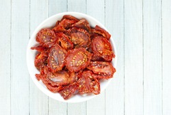 italian sun dried tomatoes in white china bowl, bright wooden table background