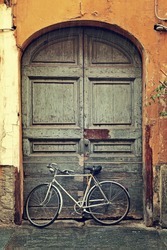 Vertical oriented image of bicycle leaning against old wooden door at the entrance to house on rainy day in Alba, Italy.