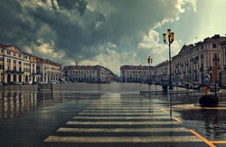 Pedestrian crossing and big plaza at city center under cloudy sky at rainy day in Cuneo, Italy.